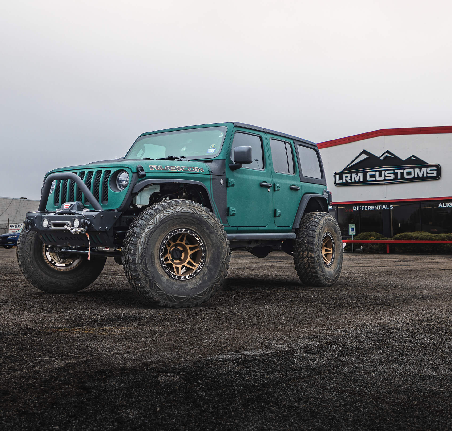 turquoise jeep, rubicon, on dirt car park, cloudy background